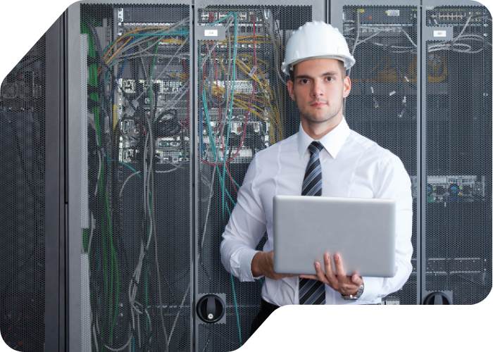 A man wearing a hard hat is holding a laptop, focused on his work in a construction or industrial setting