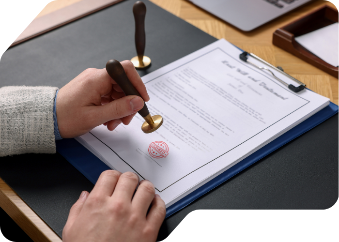 A person signing a document on a wooden desk, with a pen in hand and papers spread out
