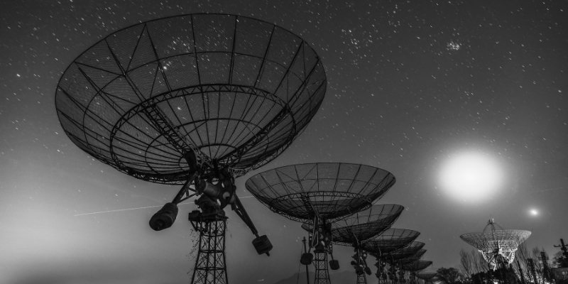 Satellite dishes silhouetted against a night sky illuminated by a full moon_gray